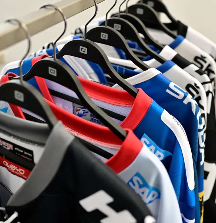 Une rangée de maillots de sport colorés personnalisés de la marque owayo est suspendue sur des cintres noirs sur un portant.