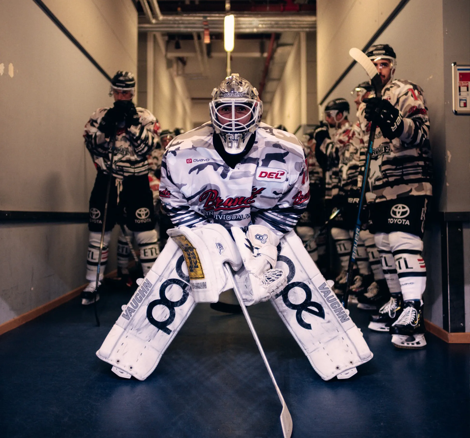 Un gardien de but de hockey dans un uniforme frappant se tient prêt, tandis que d'autres joueurs attendent derrière lui.