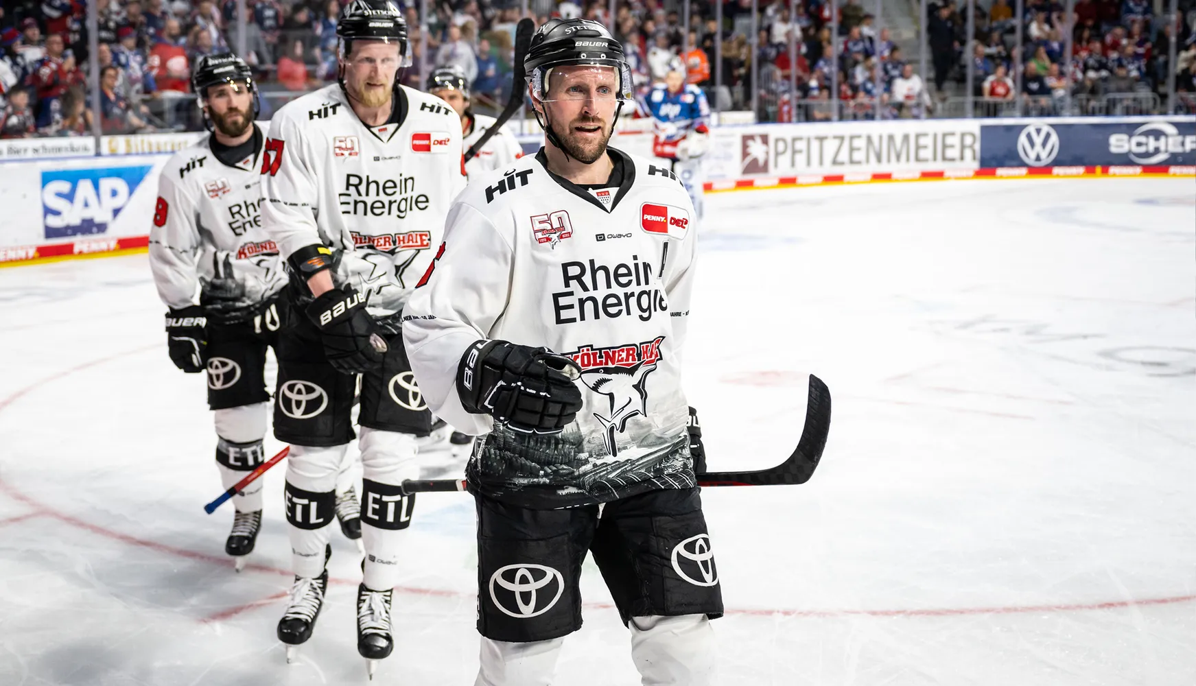 Trois joueurs de hockey sur glace en maillots blancs avec des numéros différents se tiennent sur la glace pendant un match.