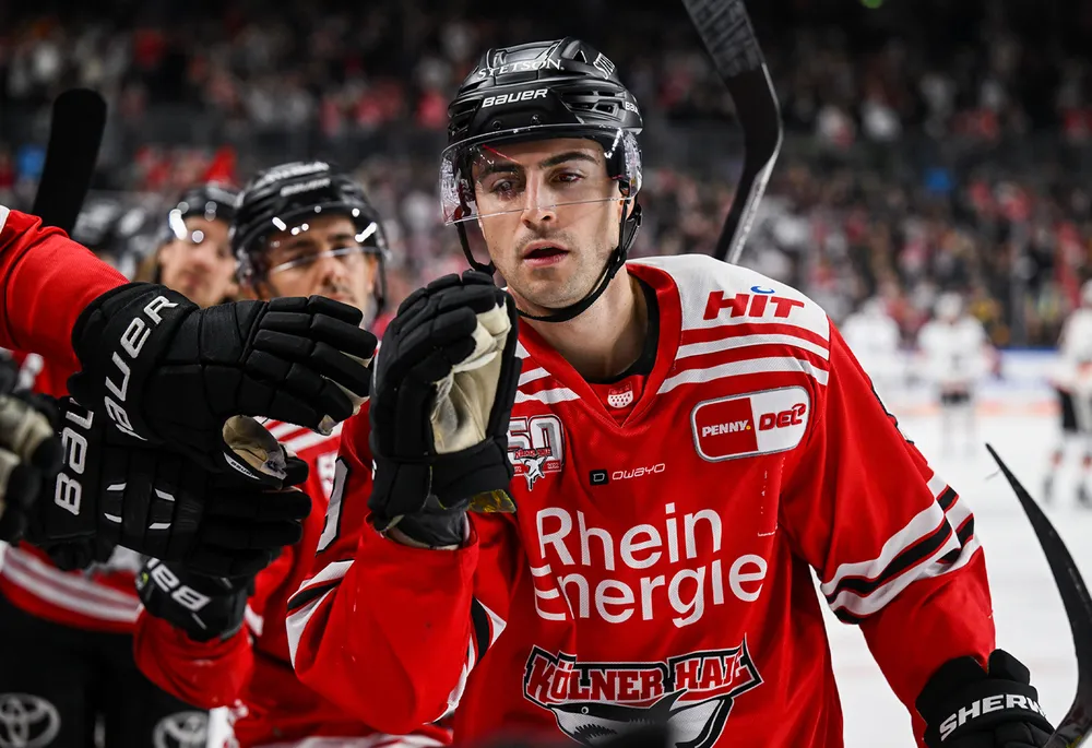 Un joueur de hockey sur glace en maillot rouge avec des gants noirs et un casque, célébrant avec ses coéquipiers.