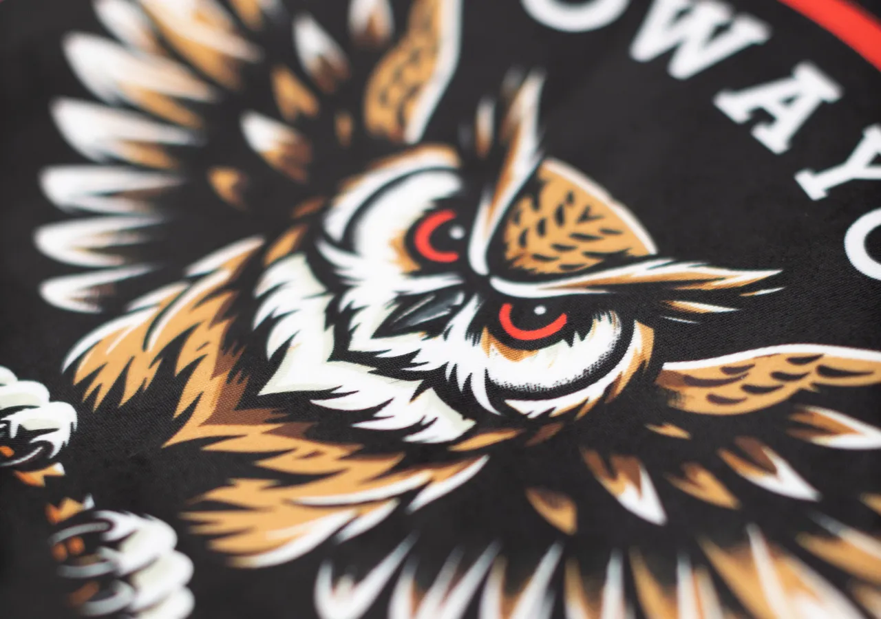 Gros plan d'un motif de hibou détaillé sur un tissu noir, symbolisant la force et la dynamique.