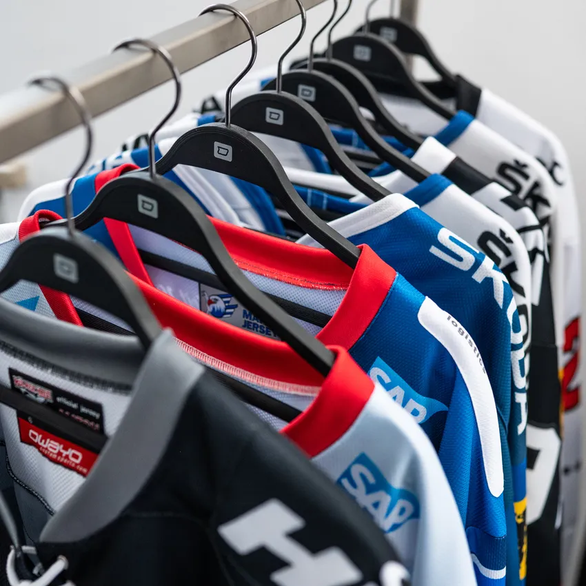 Une rangée de différents maillots de sport colorés suspendus à un cintre.