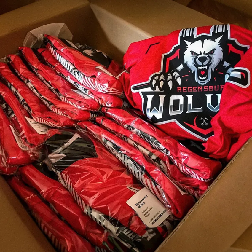 Une boîte remplie de vêtements de sport rouges avec un logo de loup et divers articles de vêtements emballés dans un film transparent.