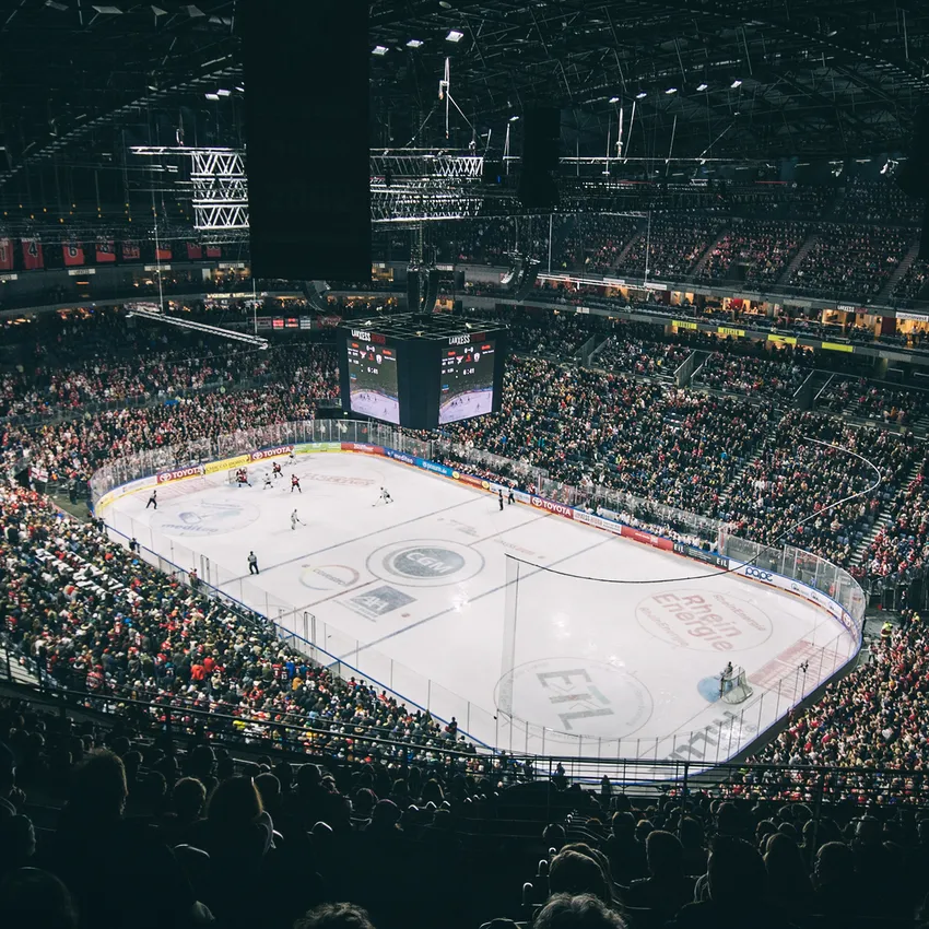 Une patinoire de hockey sur glace pleine pendant un match, avec des joueurs sur la glace et un grand tableau d'affichage en arrière-plan.