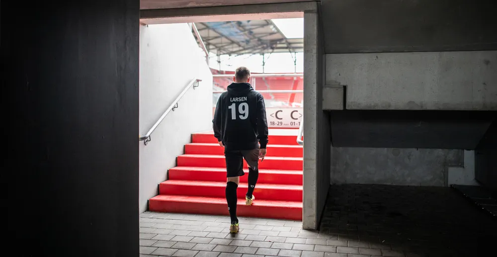Un athlète portant un hoodie noir avec le numéro 19 et un short noir montant un escalier rouge dans un stade.