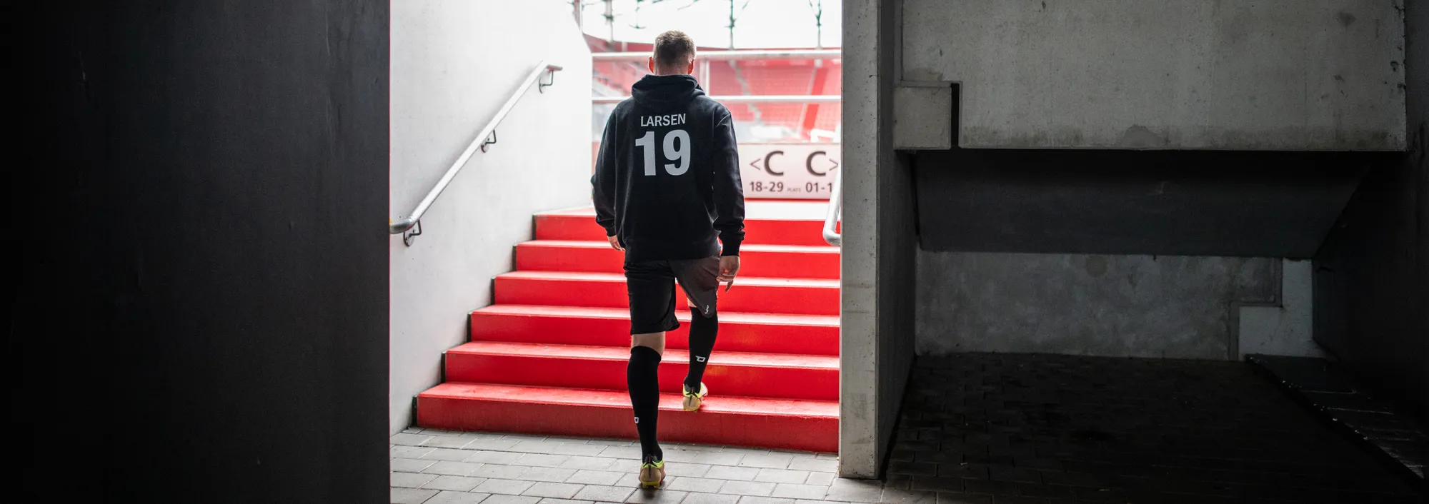 Un athlète descend les escaliers dans une tenue de sport, se dirigeant vers le terrain.