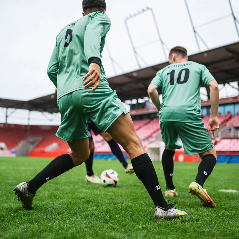 Deux footballeurs en maillots verts et chaussettes noires jouant activement sur un terrain de gazon dans un stade.
