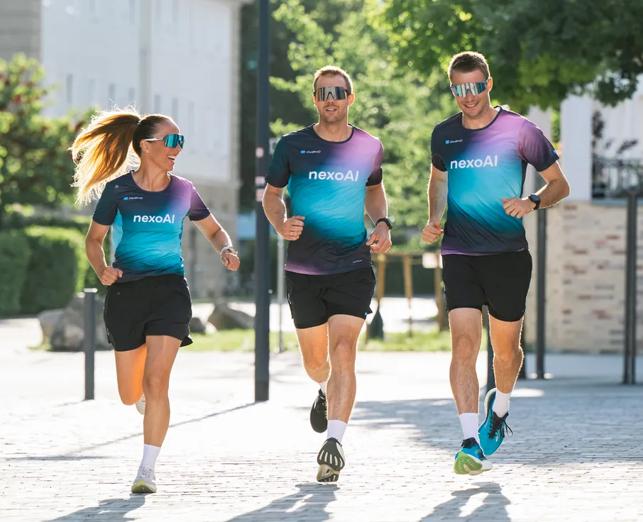 Trois athlètes, deux hommes et une femme, courent en t-shirts de course colorés assortis et en shorts sur un chemin pavé.