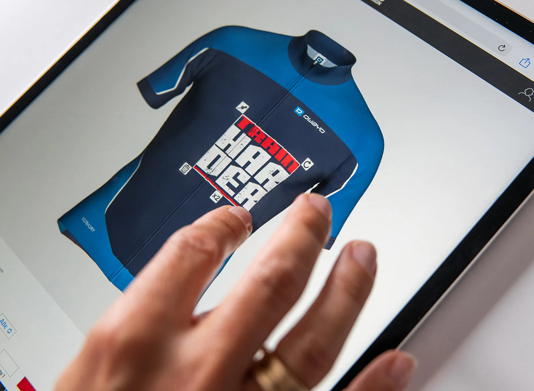Une main pointe vers un design numérique d'un maillot de sport bleu avec le texte 'train harder'.