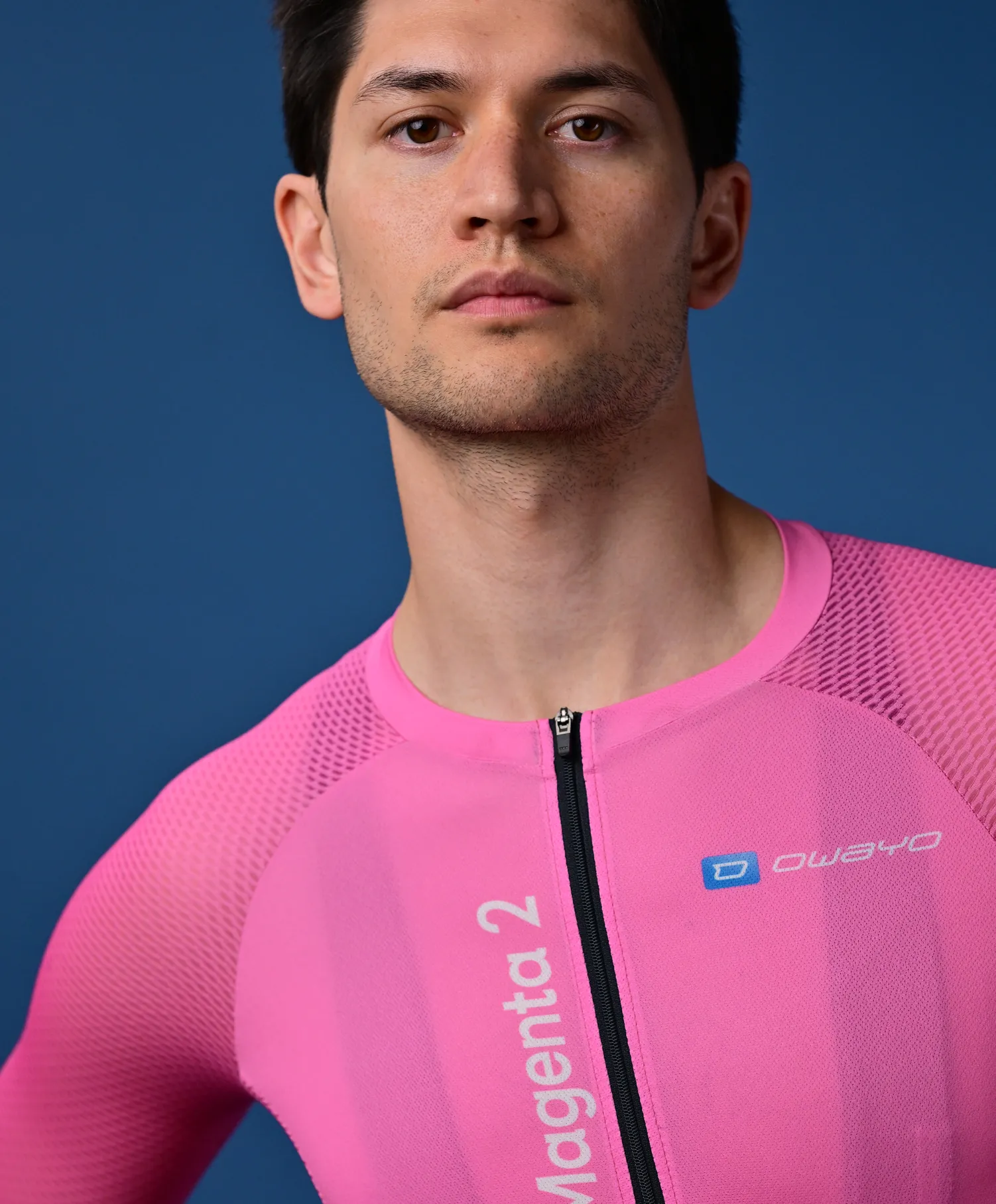 Un homme porte un maillot de sport rose sans manches avec une fermeture éclair et le logo 'owayo' sur la poitrine.