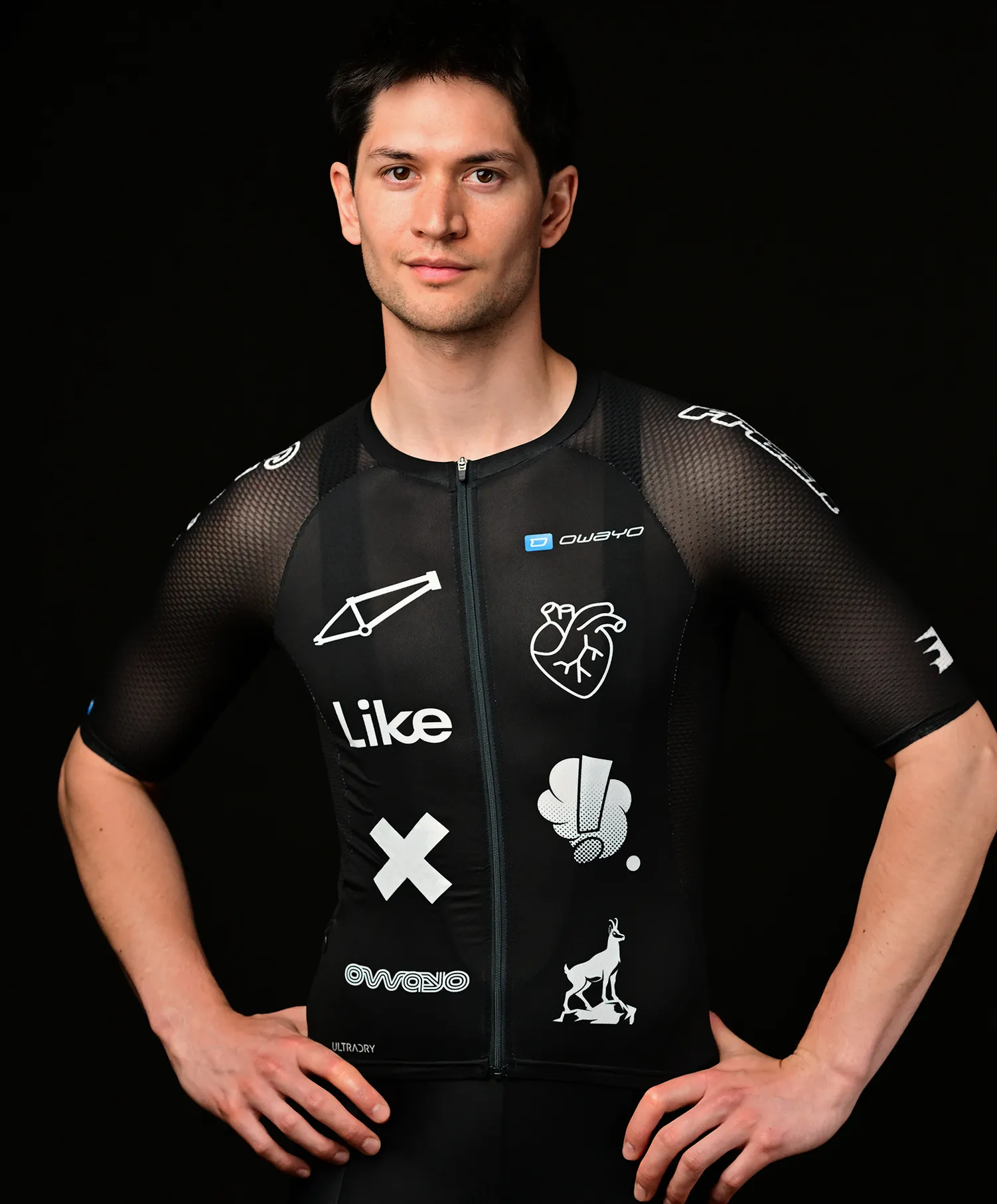 Un homme portant un maillot sportif noir personnalisé par owayo avec divers motifs blancs, notamment un cadre de vélo, un cœur, un 'X', une main faisant un pouce levé, un animal et le mot 'Like'.