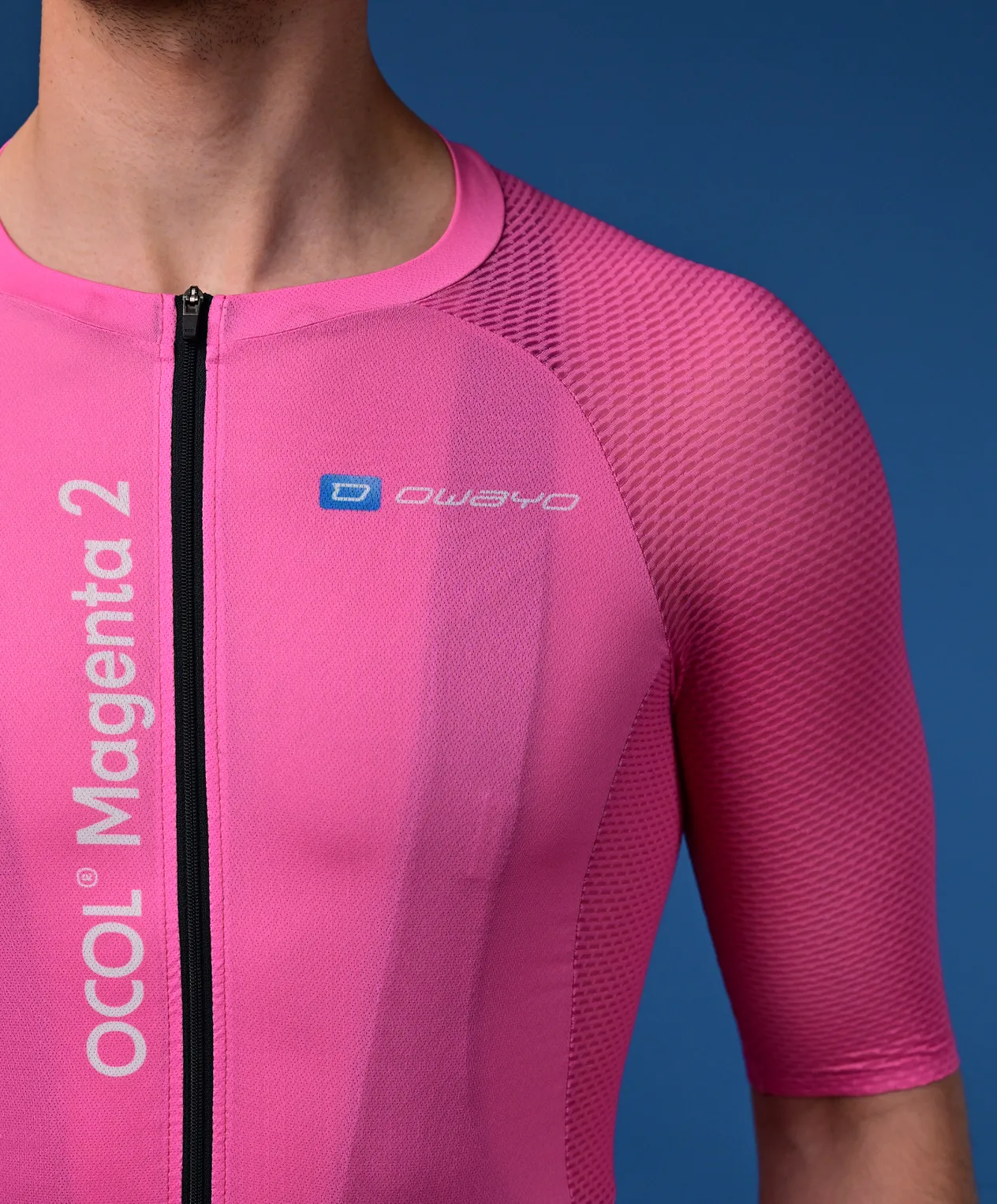 Un homme porte un maillot de cyclisme rose à manches courtes avec une fermeture éclair noire et le logo 'owayo' sur la poitrine. Sur le côté gauche, il est écrit verticalement 'OCOL Magenta 2'.