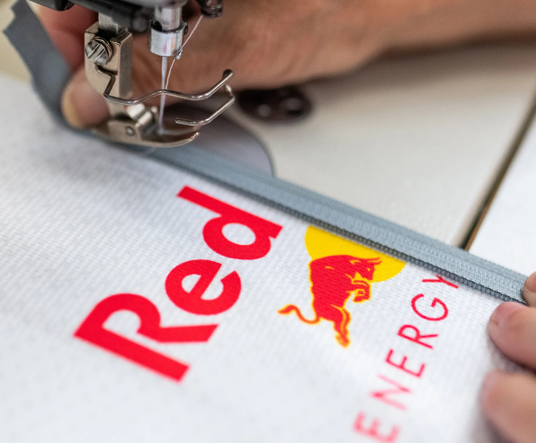 Une machine à coudre fixe une fermeture éclair grise sur un vêtement de sport blanc portant le logo Red Bull.