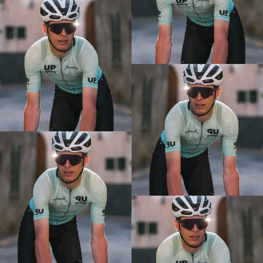 Un cycliste portant un maillot à manches courtes bleu clair et un short noir roule sur une rue ensoleillée.