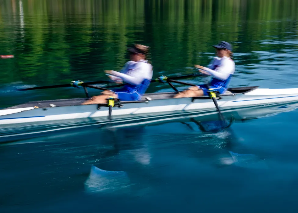 Deux rameurs en vêtements de sport bleus rament en synchronisation sur une eau calme.