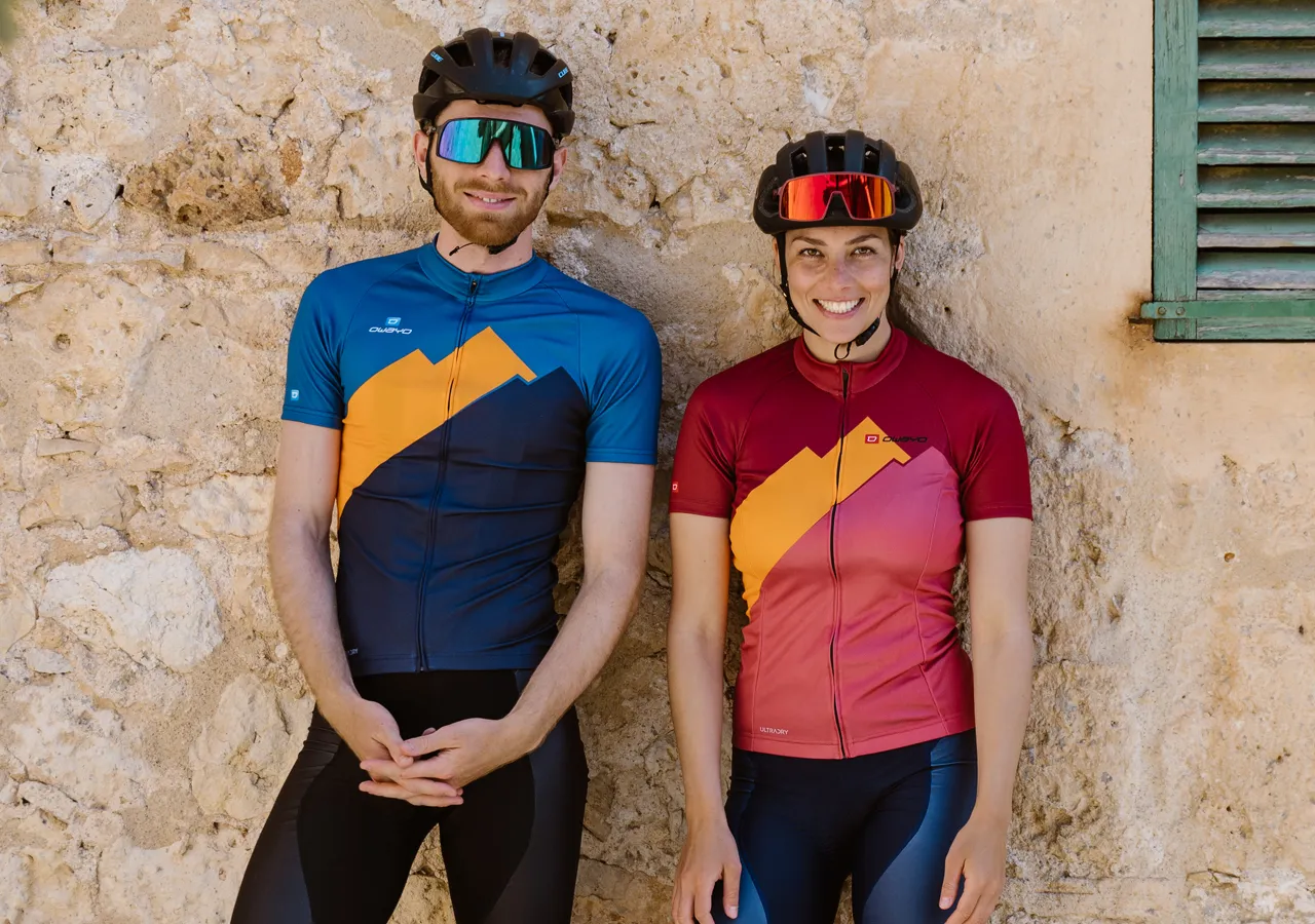 Un homme et une femme en tenues de sport personnalisées d'owayo, debout devant un mur de pierre.