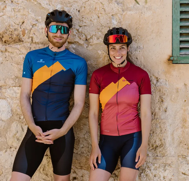 Un homme et une femme portant des maillots de cyclisme personnalisés d'owayo, debout devant un mur de pierre.
