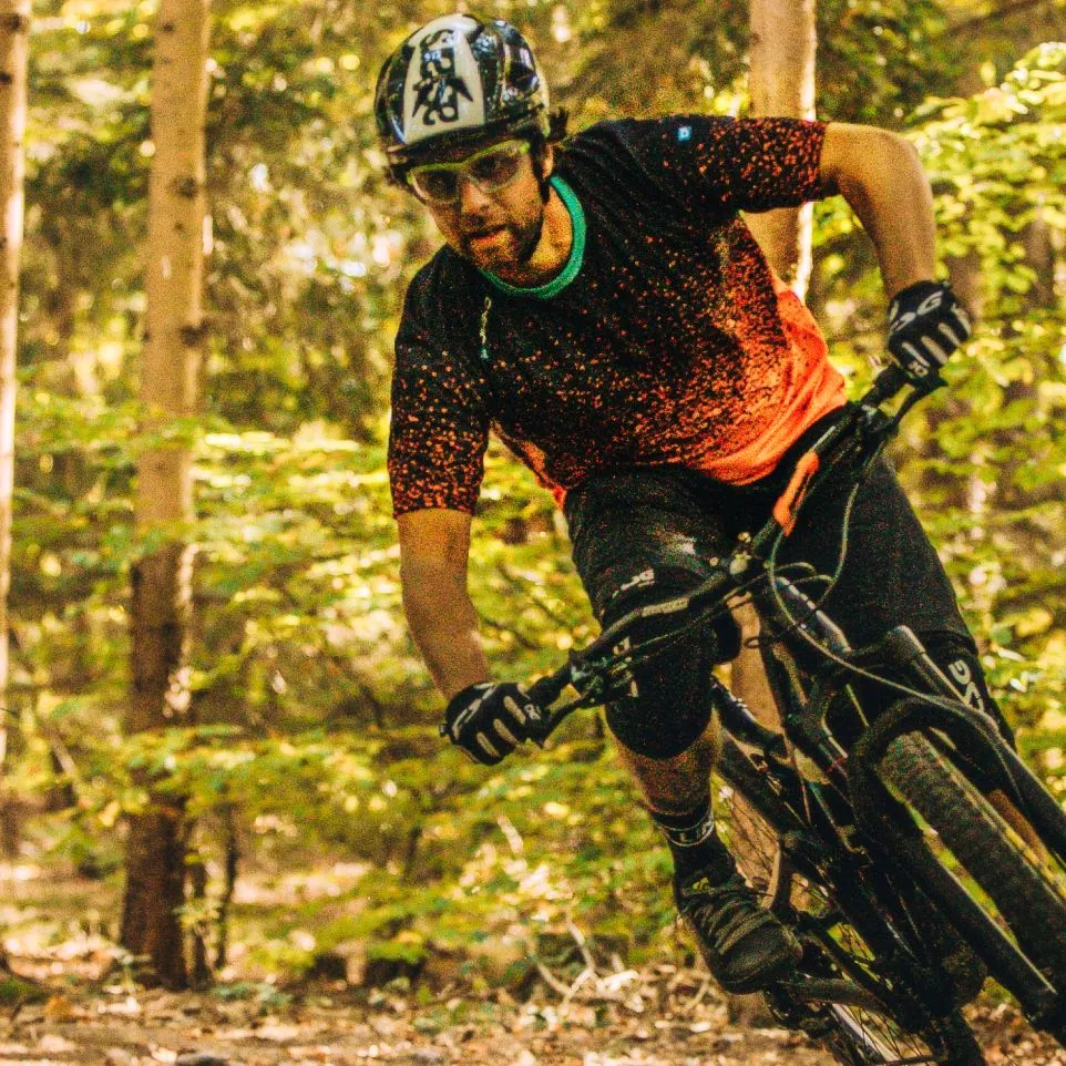 Un cycliste de montagne portant un maillot noir à motifs rouges et un short noir roule dans une forêt.
